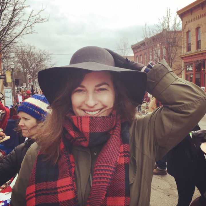 photo of a woman with brown hair smiling while holding the big, black hat on her head