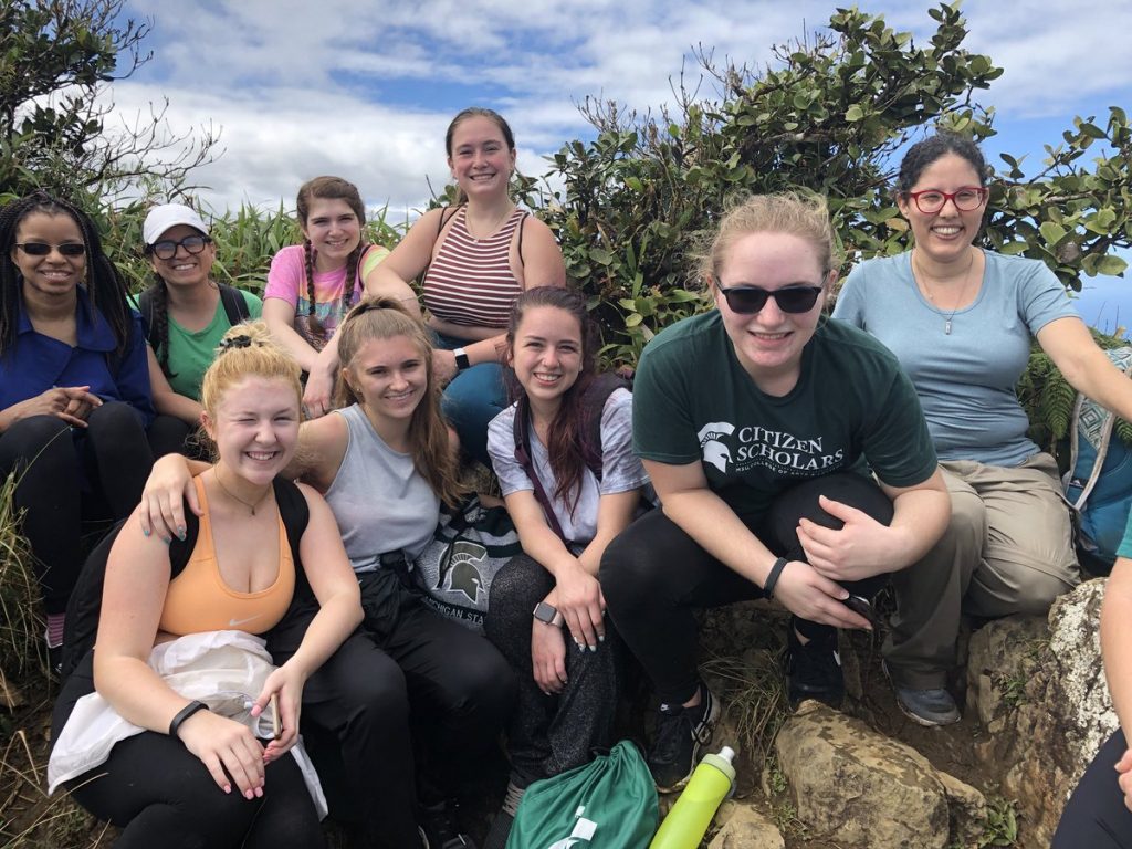 Group of nine women posing for a picture in front of greenery