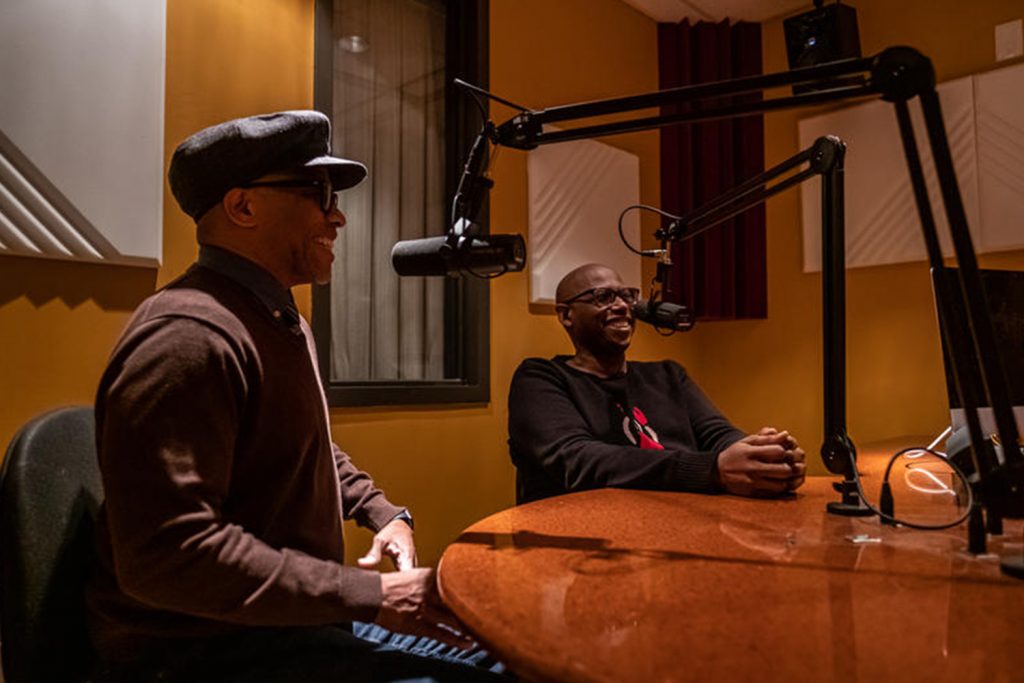 two men in a sound booth talking into microphones 