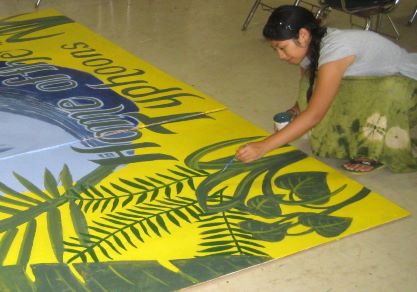 Woman wearing a white shirt painting a yellow mural on the ground