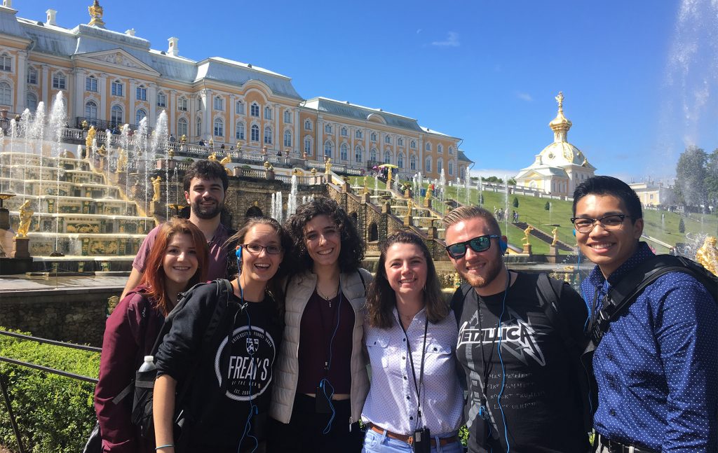 group of people smiling for a picture in front of white buildings in Russia