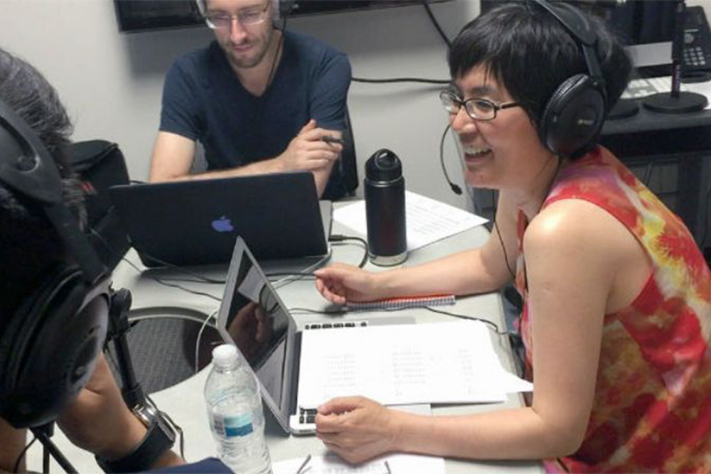 three people sitting at a small table with laptops and headphones