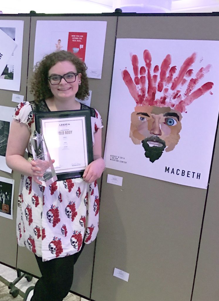 woman posing next to her poster with her two awards