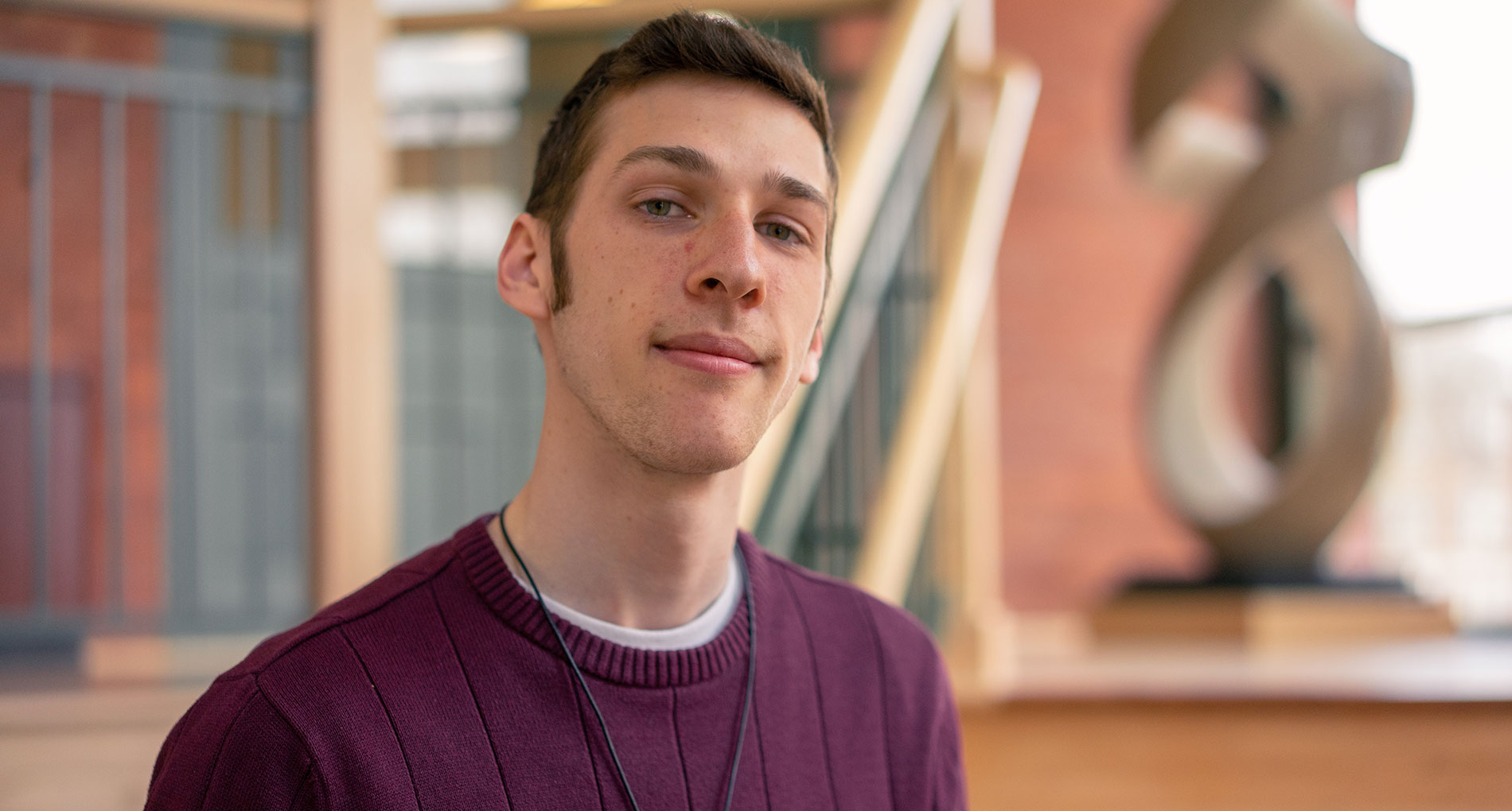 Portrait shot of a man with brown hair wearing a deep purple colored sweater and necklace