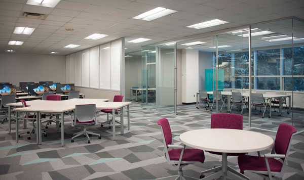 view of meeting space in the lab, tables with pink chairs and computers in the background