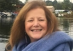 a women with brown hair wearing a purple sweater with water behind her