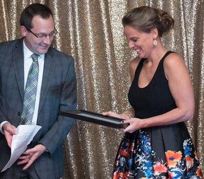 woman in dress receiving award from man with glasses