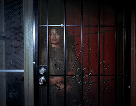 one of jarod lew's photographs featuring a woman behind a screen door