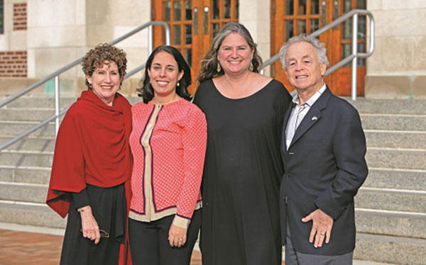 three women and a man standing together posing in front of staircase smiling