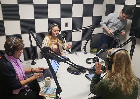 Group of four people in a studio sitting at a table with microphones