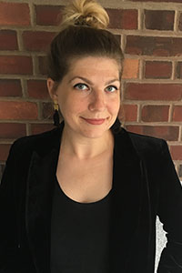 woman with her hair up in a bun who's wearing a black shirt and suit jacket who's looking at the camera