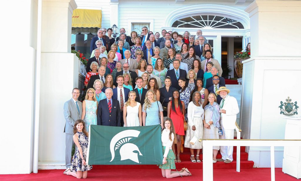 Arts weekend attendees in front of hotel entrance and man holding Spartan flag