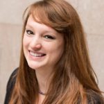 headshot of a woman with long hair and bangs. she is smiling and wearing a top and cardigan