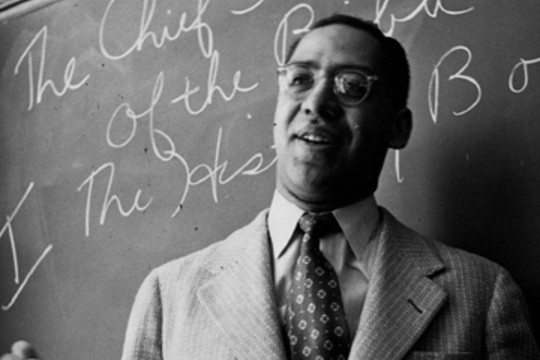 a black and white image of a man in a suit standing in front of a chalk board