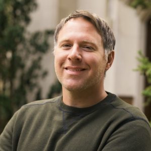 Man with brown-grey hair wearing a green sweater.