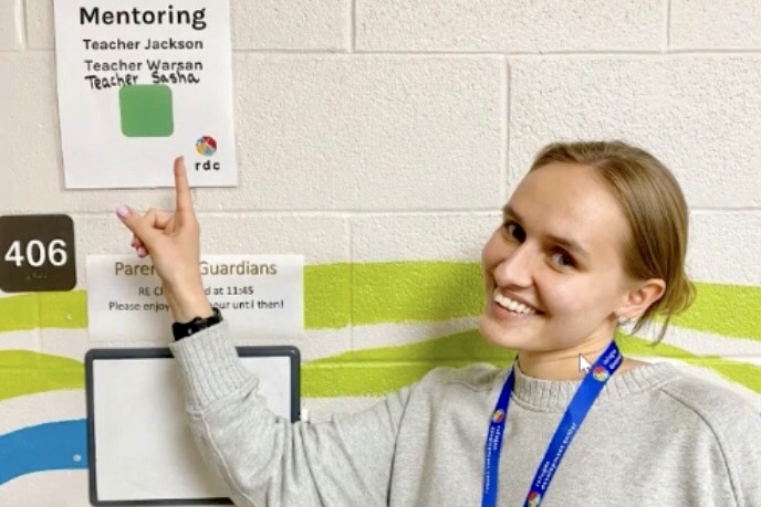 Person pointing at sign on white brick wall.