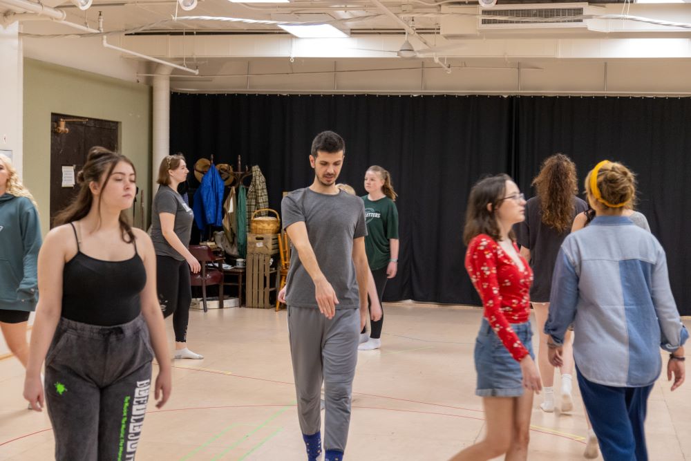 A group is students follow a movement instructor while walking around the room in different styles.