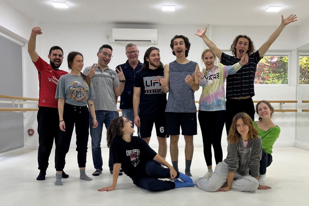 A group of 11 people in a dance studio space.