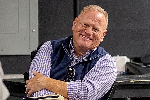 Larry Joe Campbell smiling warmly, sitting in a chair with his arms crossed. He is wearing a purple and white button up shirt with a dark blue vest.