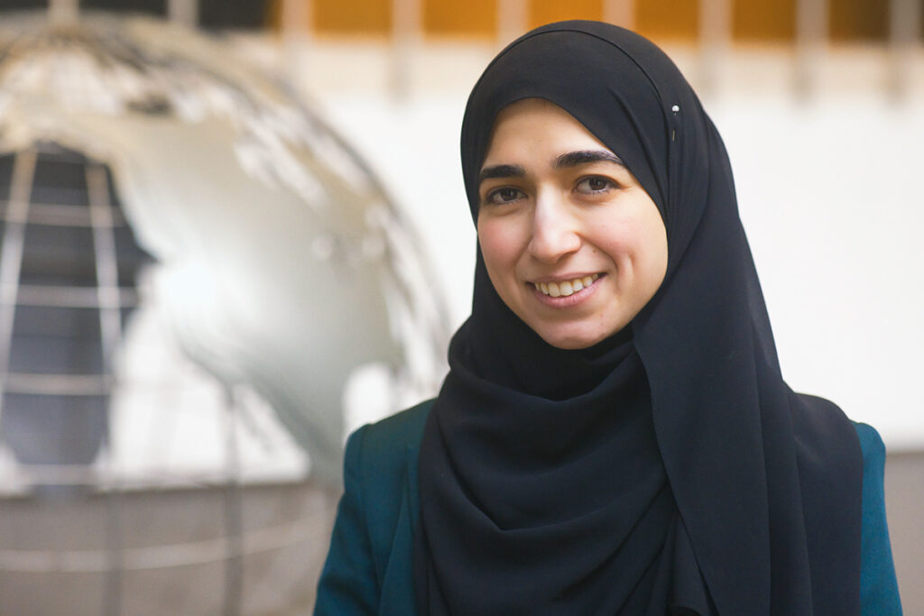 A woman in a black headscarf, MSU Assistant Professor Nareman Amin, stands by a globe sculpture in the MSU International Center in East Lansing, Michigan.