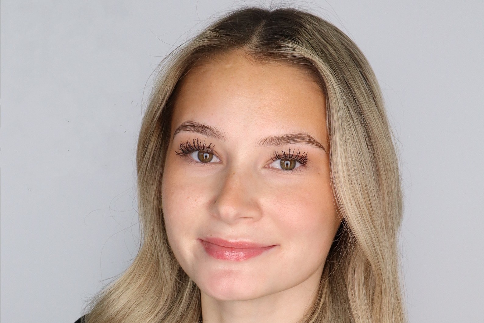 Professional headshot of a woman with long blonde hair wearing a black blazer and light-colored top, facing the camera against a light gray background.