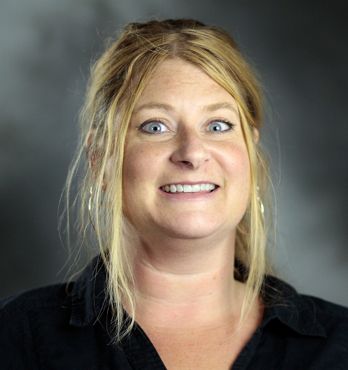 Headshot photo of a woman with blonde hair that is pulled back. Hse is smiling and wearing a black shirt. 