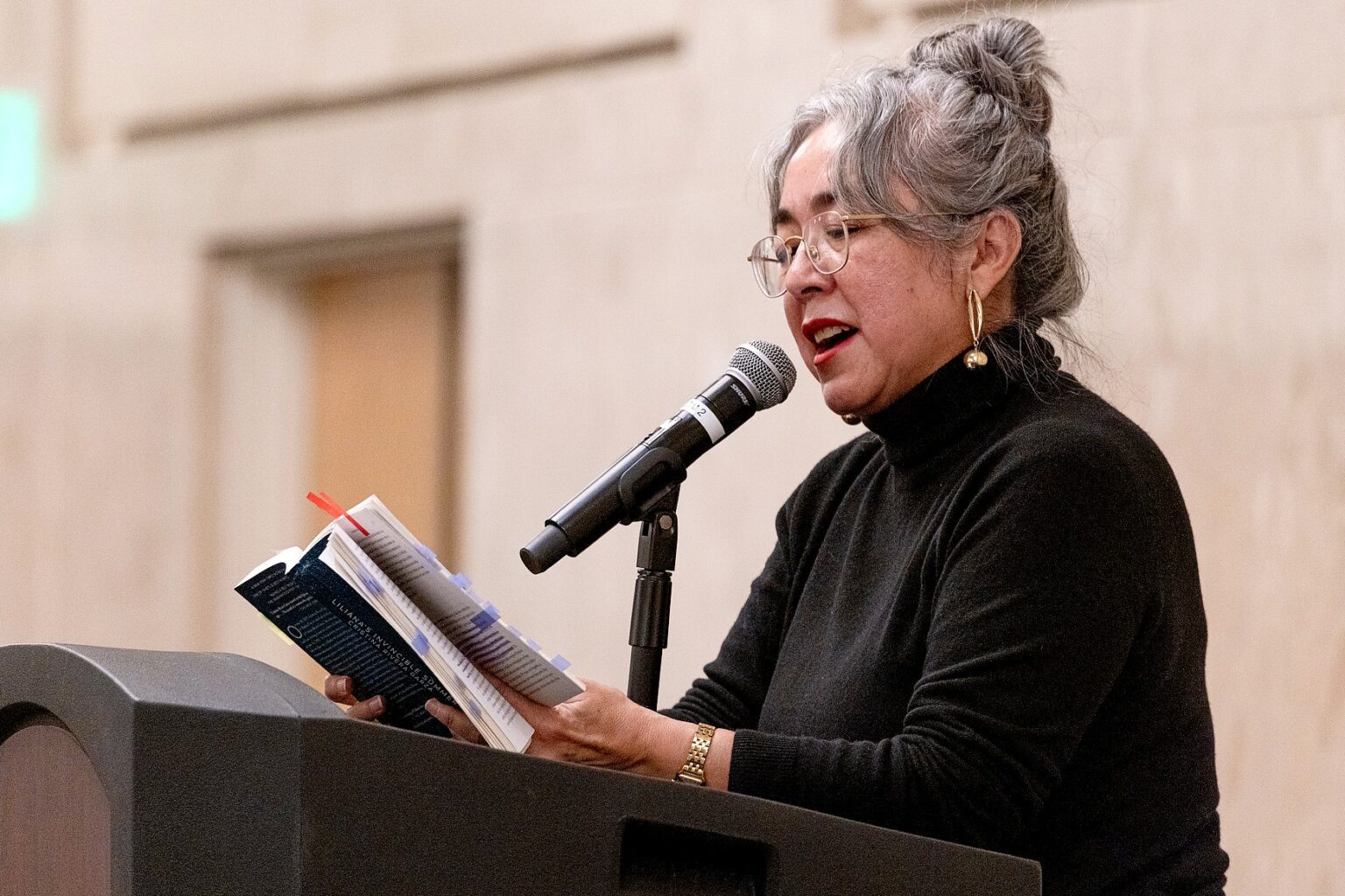 Cristina Rivera Garza stands at the podium reading aloud from her annotated copy of a book.