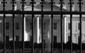 black and white photo of a fence with a house in the background