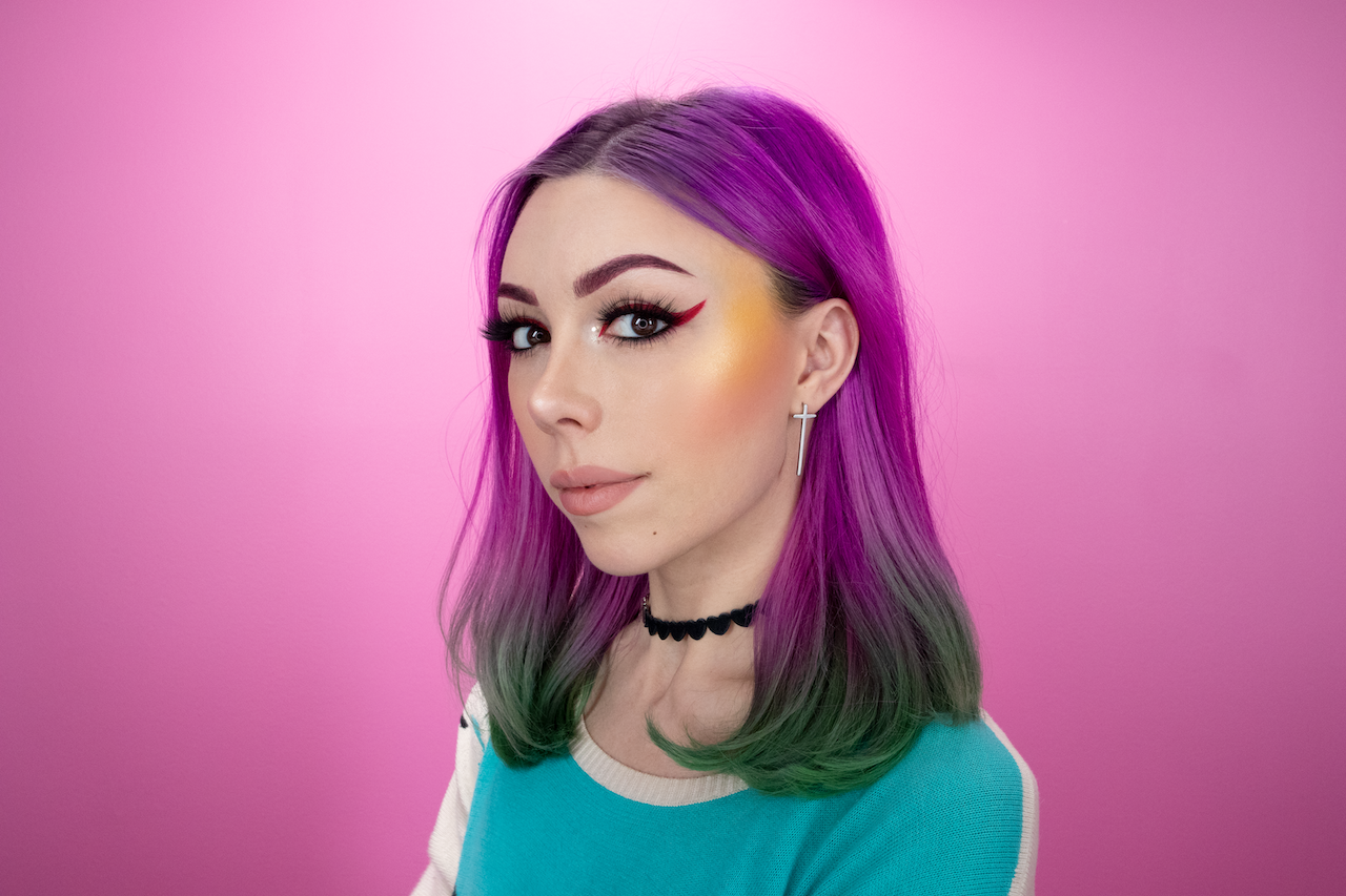 woman with purple and green hair in front of a pink background
