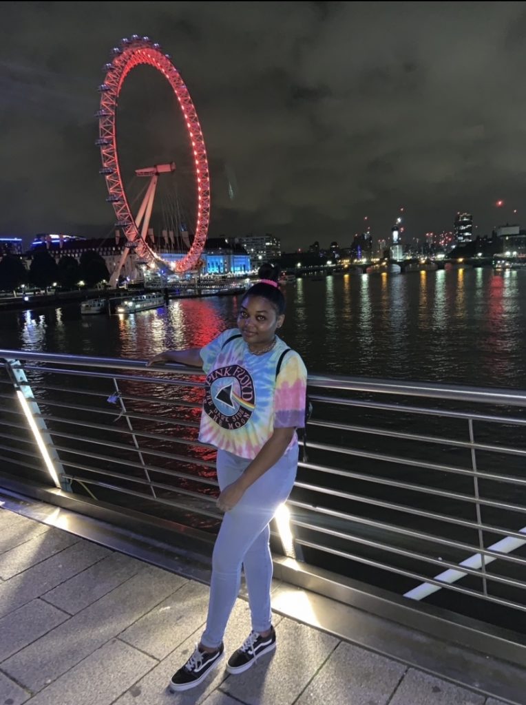 a woman in a bun and t-shirt smiling on a bridge in front of a ferris wheel