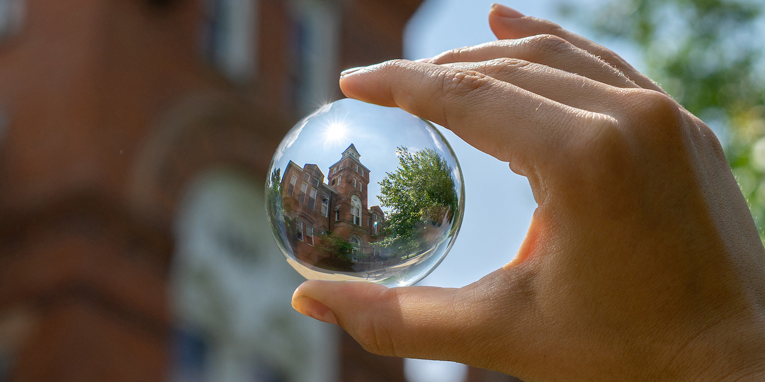hand holding a glass ball that is reflecting an orange brick building with a bell tower