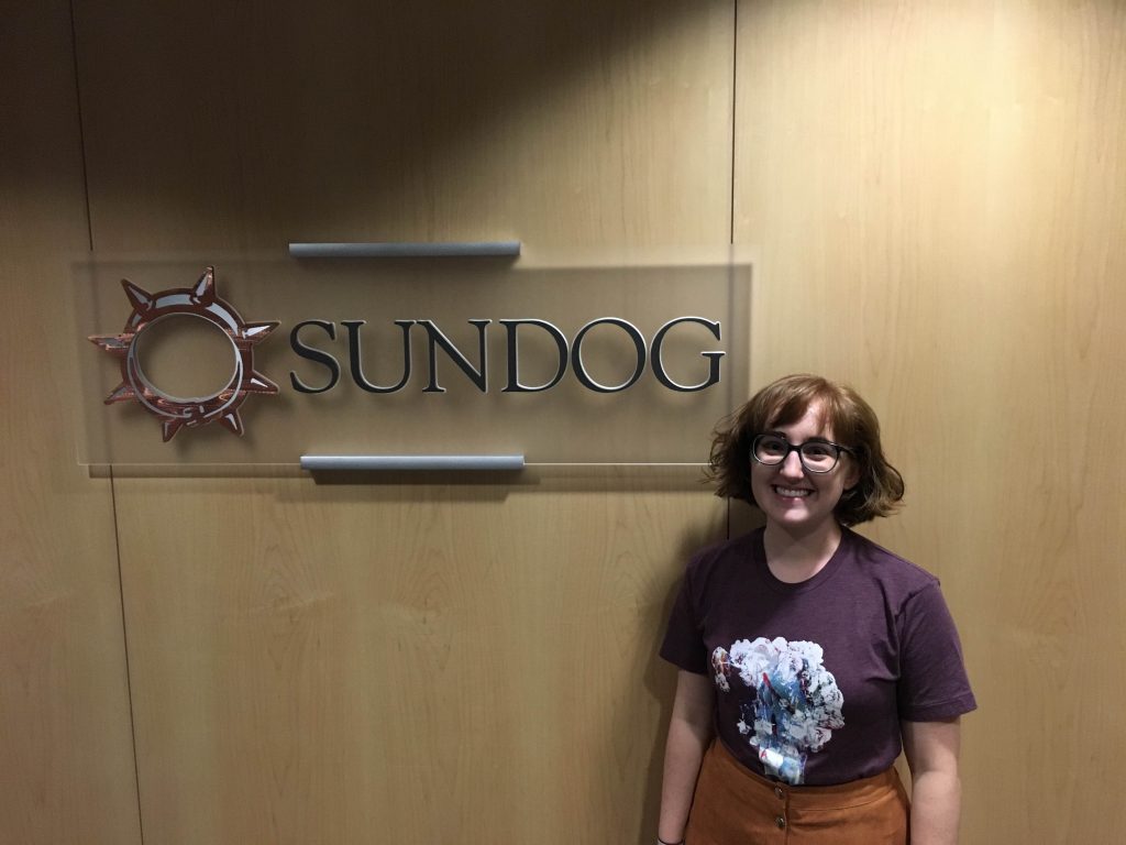 a girl with short hair in a purple shirt standing next to a sundog sign