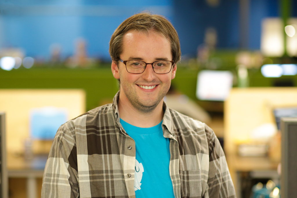 picture of a young man with blonde hair and rectangular glasses. he is wearing a teal shirt and flannel