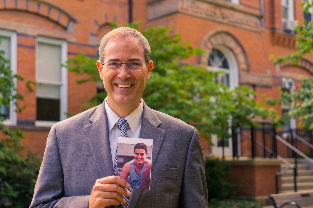 Man in a grey suit holding a photo of his younger self