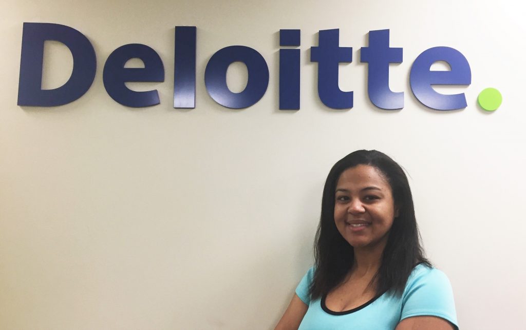 woman wearing a blue shirt standing against the wall with Deloitte written on it