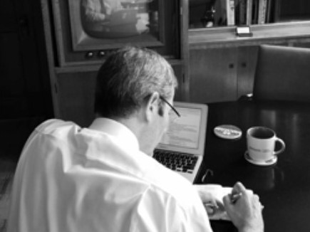 back view of man wearing a white shirt and glasses writing something on a paper