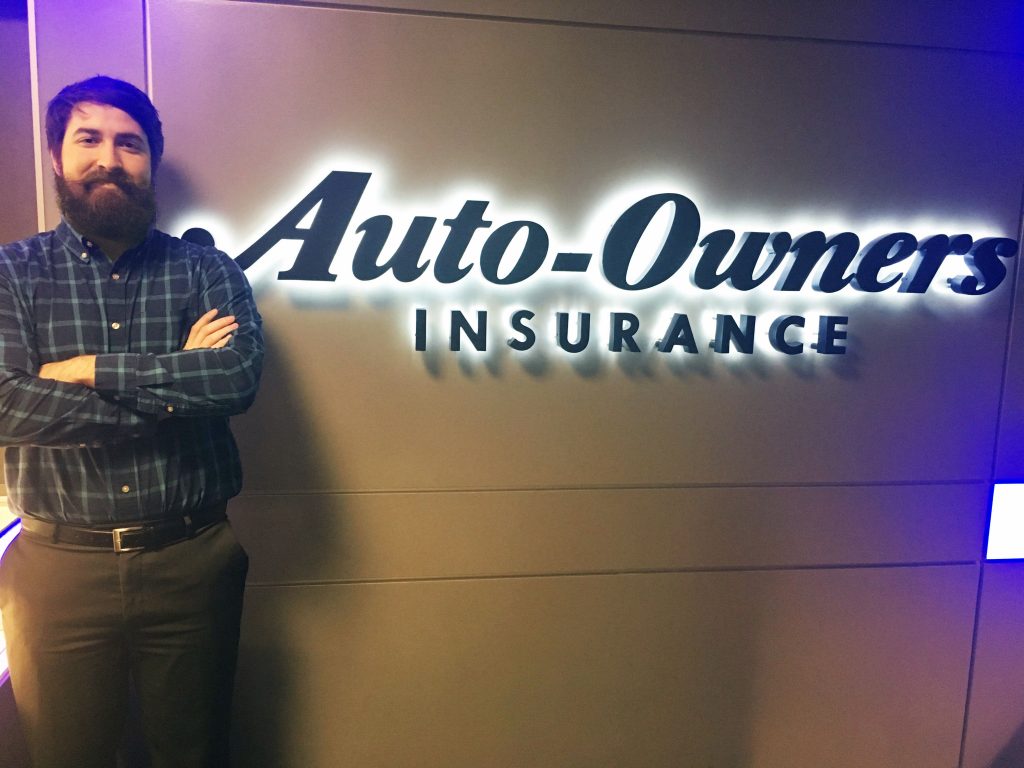 Man with brown hair standing by the Auto-Owners Insurance logo