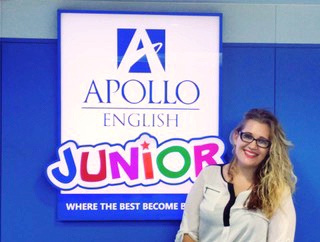 woman wearing a white top and glasses standing in front of an Apollo Junior sign