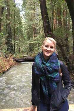 woman wearing a blue jacket and scarf standing in the middle of the woods
