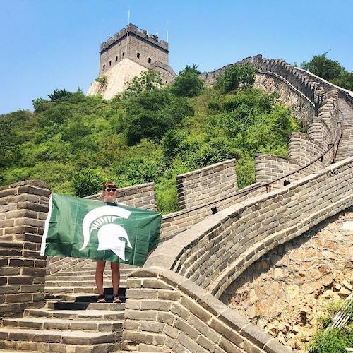 a girl on the great wall of china holding the MSU flag 