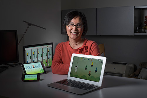a women with short hair wearing glasses and a orange shirt showing her laptop
