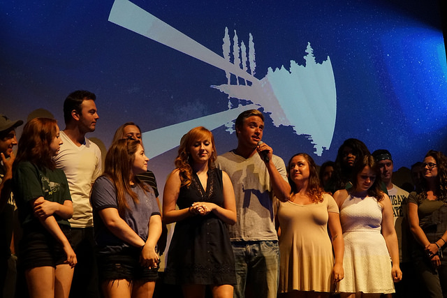 group of students on a stage, one of them singing a song