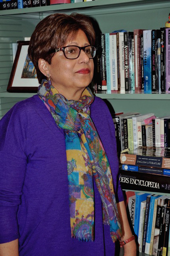 Woman with dark hair and glasses standing next to a bookshelf