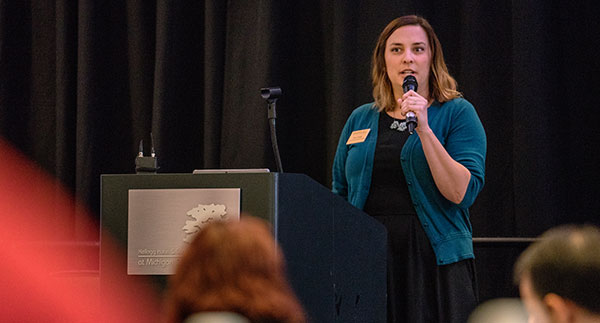 woman in black dress and teal cardigan speaking at a podium at the conference