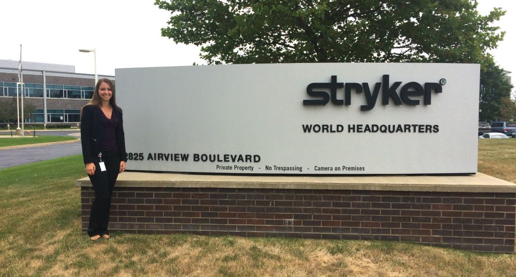 Woman standing next to a large sign for Stryker World Headquarters