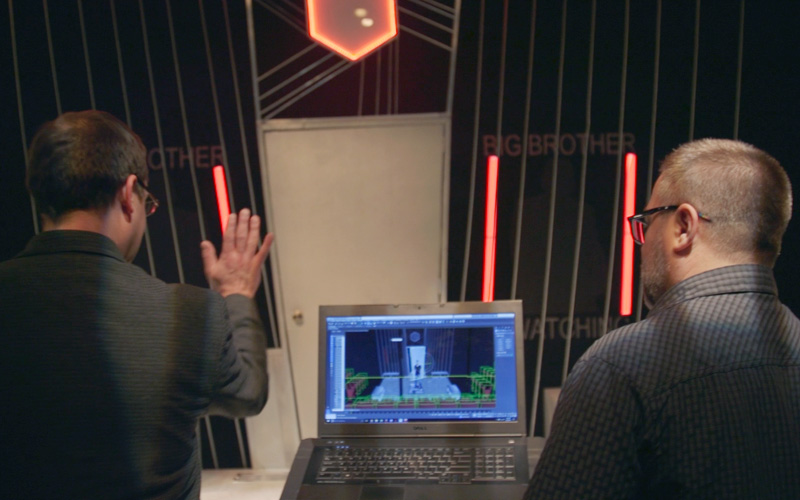 2 men with their backs to the viewer as the compare the computer model of a stage design and the actual stage.