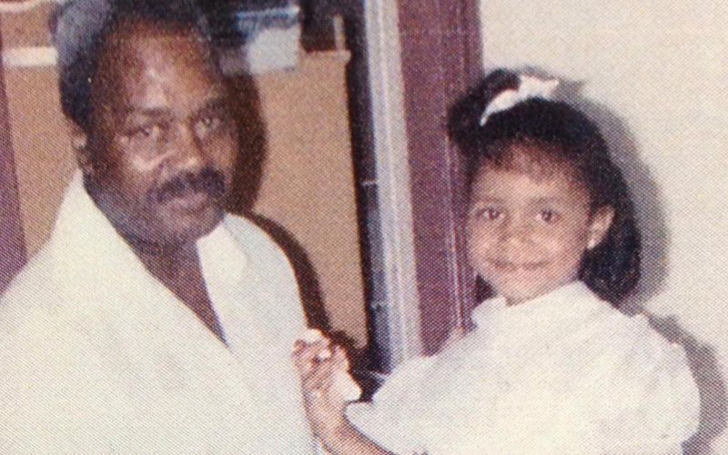 An African American father with a mustache and daughter wearing a white dress and white bow in her hair