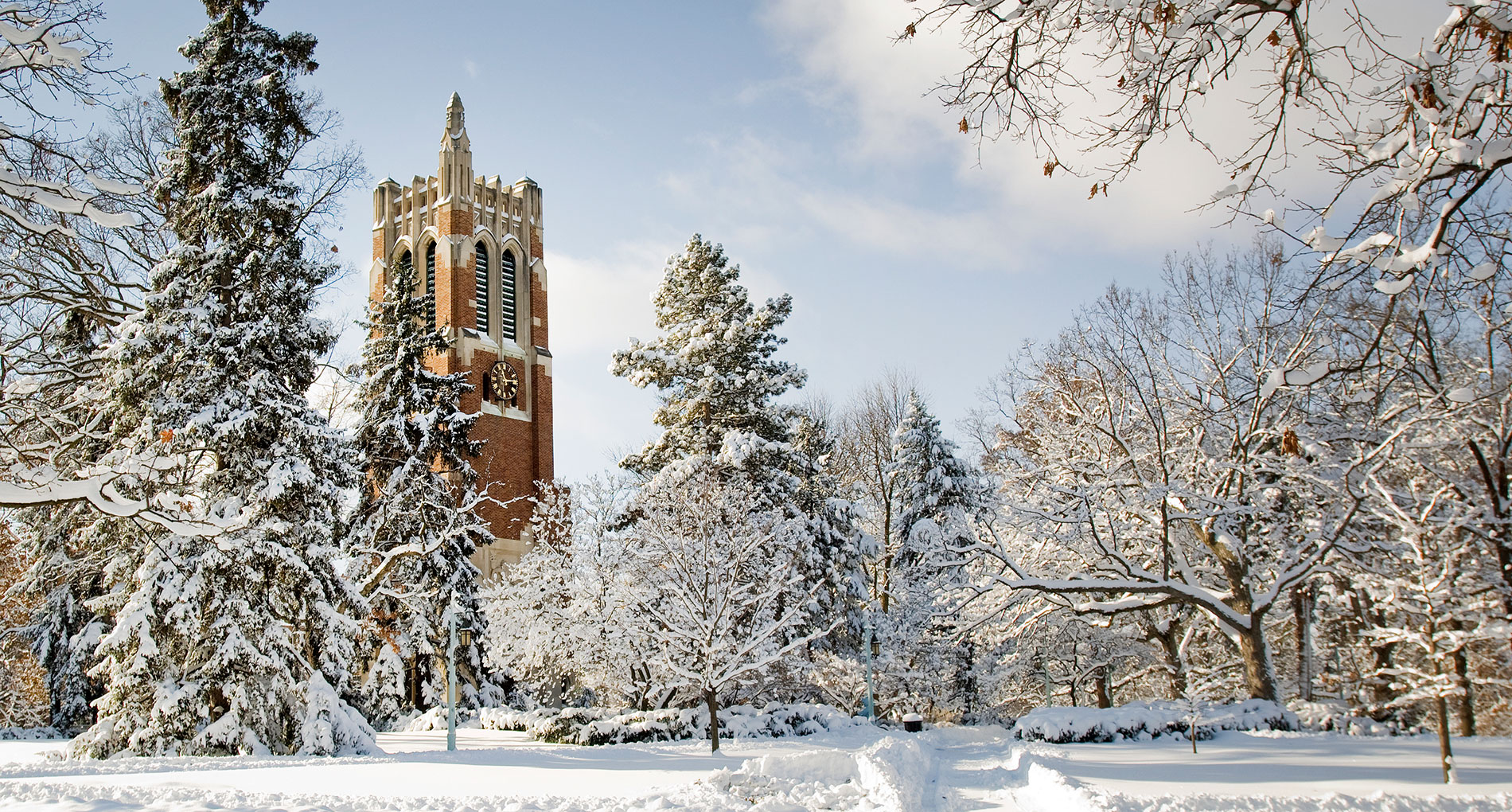 picture of the beaumont tower, made of red bricks, trees are surrounding the building with snow all around