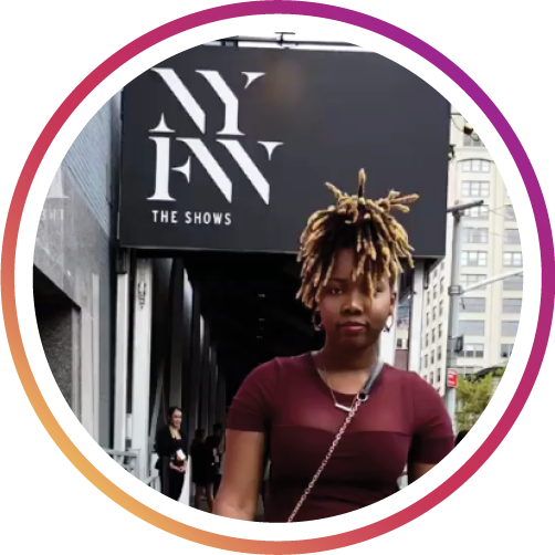 a girl with hair up in a maroon shirt standing in front on the NYFW sign