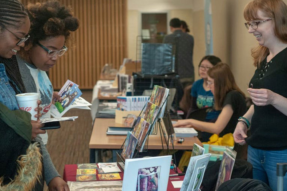 Three people standing over an organized table of comics